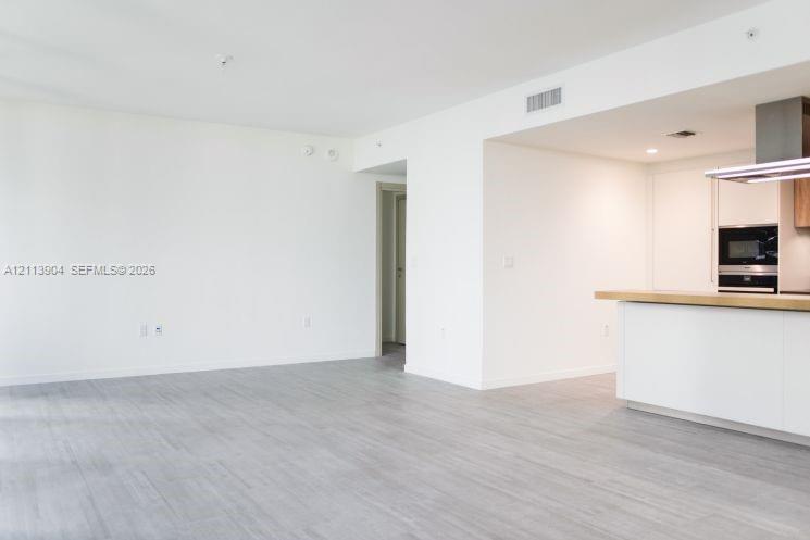 Open-concept interior featuring light wood-finish flooring, white cabinetry, a wood-topped kitchen island, and a stainless steel built-in oven and range hood