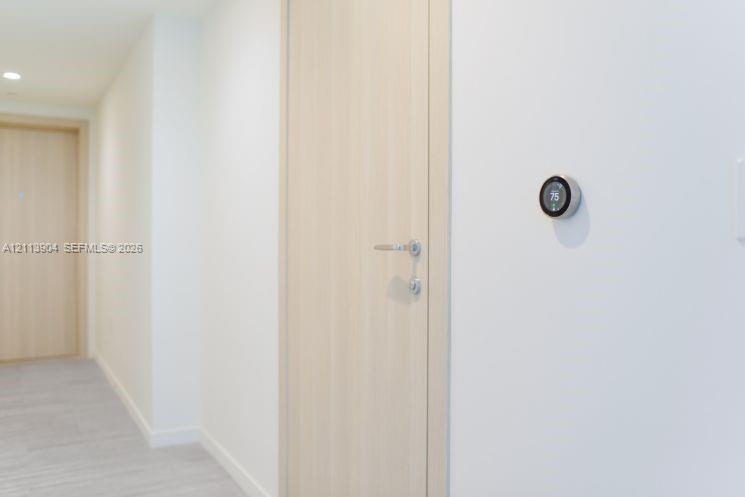 Light-toned wood-finish interior door featuring satin nickel hardware, paired with a wall-mounted smart thermostat and recessed ceiling lighting