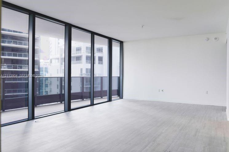 Floor-to-ceiling windows featuring dark frames, wood-finish flooring, and a glass-paneled exterior balcony
