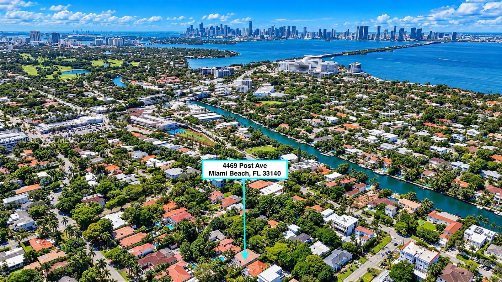 Aerial perspective of a residential property situated in a coastal environment featuring dense mature canopy, proximity to a waterway, and a coastal city skyline
