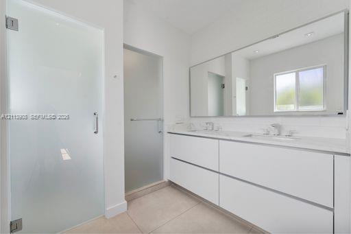 Bathroom featuring a dual-sink floating vanity with white cabinetry, a full-width wall mirror, oversized tile flooring, and frosted glass door enclosures