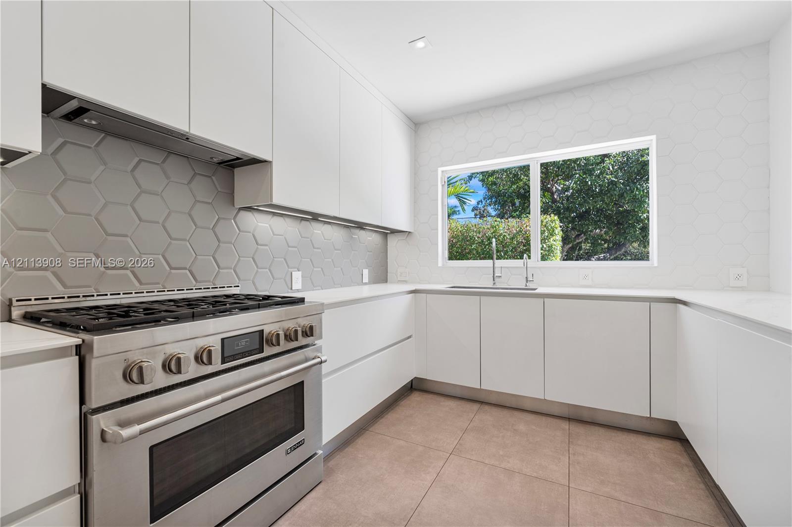 Modern kitchen featuring flat-panel cabinetry, a professional-grade stainless steel range, hexagonal tile backsplash, light-toned stone countertops, and large-format tile flooring