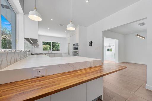 Kitchen featuring a waterfall-edge countertop, butcher block peninsula, geometric tiled backsplash, recessed lighting, and stainless steel built-in double wall ovens