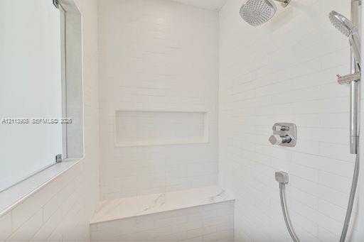 Walk-in shower featuring white subway-style wall tile, a stone-finish bench seat, an integrated wall niche, and dual-function polished chrome shower fixtures