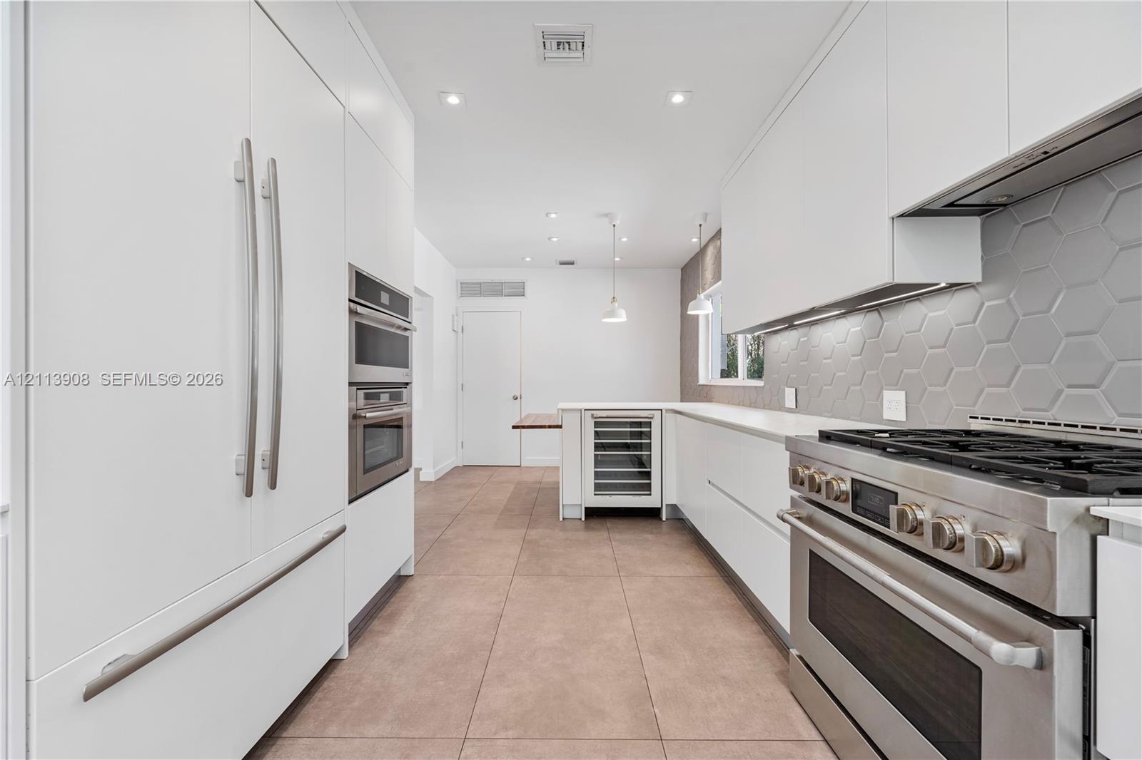 Contemporary kitchen featuring flat-panel white cabinetry, stainless steel professional-grade range, hexagonal tile backsplash, built-in wine refrigeration, and large-format tile flooring