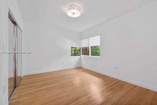 Room featuring wood-finish flooring, corner windows with fitted shades, a decorative flush-mount ceiling fixture, and a mirrored sliding-door closet