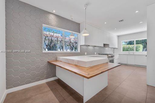 Kitchen featuring matte white flat-panel cabinetry, hexagonal-patterned accent wall, stone-topped island with wood-finished breakfast bar, and tile flooring