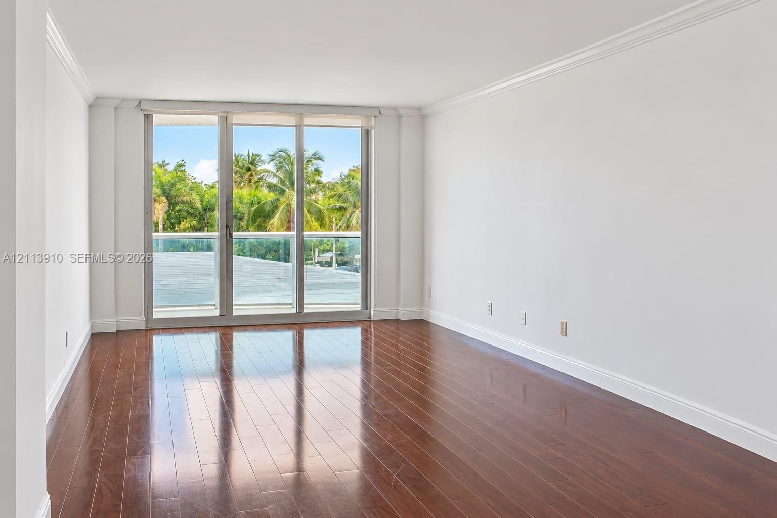 Open-concept interior featuring wood-finish flooring, crown molding, and floor-to-ceiling glass sliding doors leading to a balcony with a glass railing Open-concept interior featuring wood-finish flooring, crown molding, and floor-to-ceiling glass sliding doors leading to a balcony with a glass railing