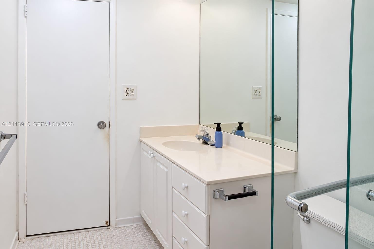 Bathroom featuring a solid-surface vanity countertop, integrated sink, white cabinetry with drawers, large wall-mounted mirror, and glass-enclosed shower stall with a grab bar