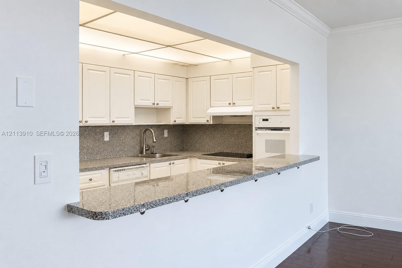 Kitchen featuring white cabinetry, stone-finish countertops, an integrated cooktop, a built-in oven, and an extended breakfast bar
