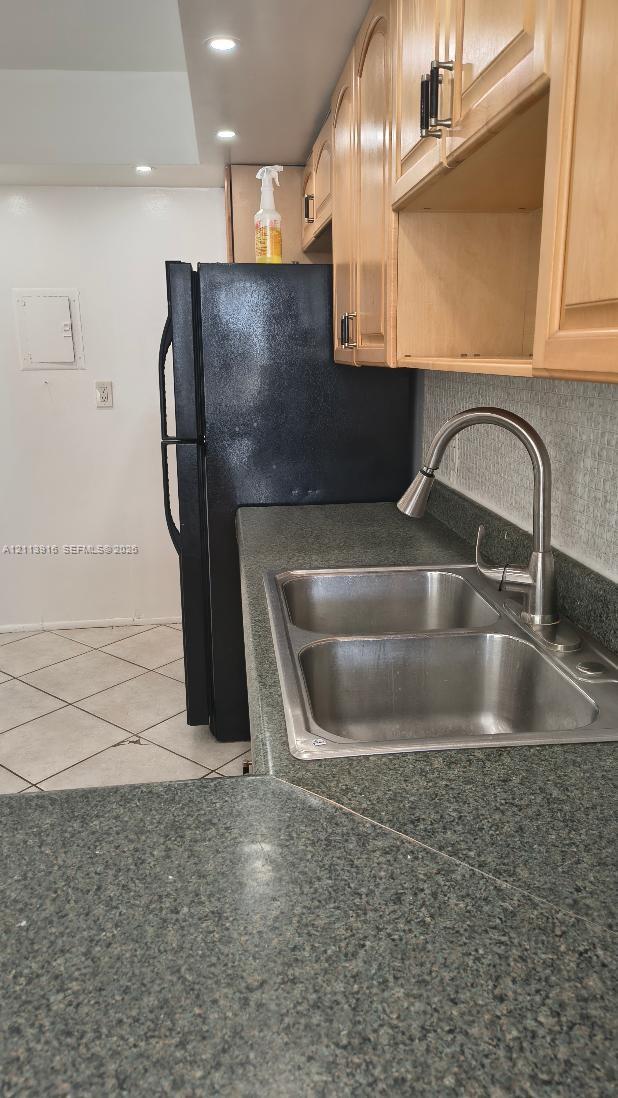 Kitchen featuring wood-finish cabinetry, stone-texture laminate countertops, a stainless steel double-basin sink with a pull-down faucet, a built-in black refrigerator, and tile flooring