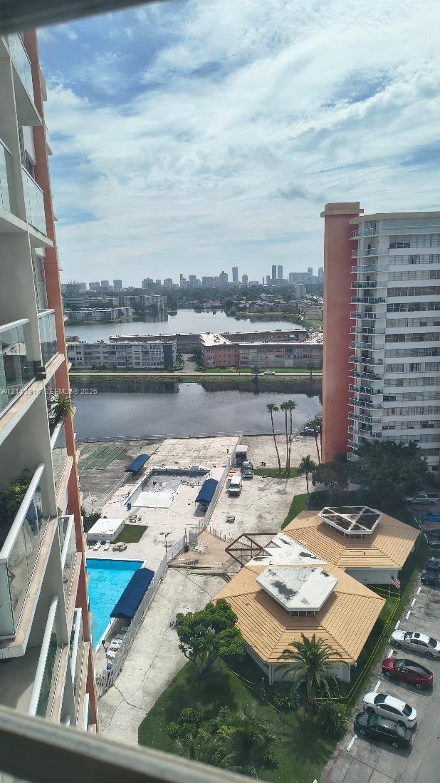 High-rise exterior with glass-panel balcony railings, swimming pool, and landscape area featuring palm trees and tile-roof pavilions