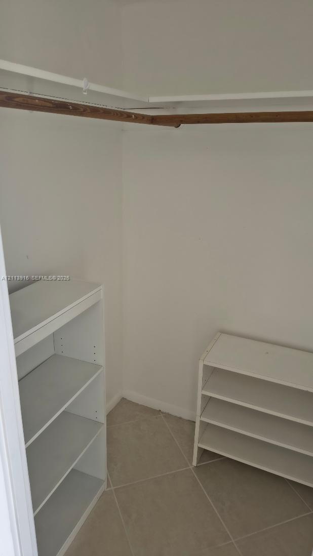 Storage space featuring tile flooring, built-in shelving units, and an overhead closet rod