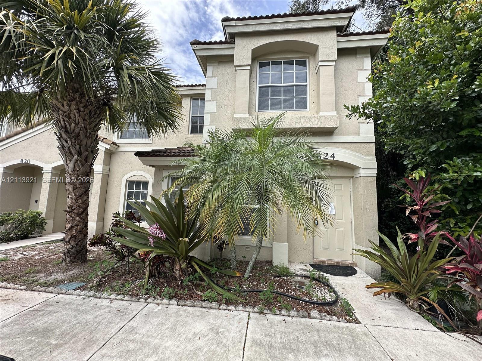 Two-story stucco exterior featuring arched entryways, decorative corner quoins, tile roof accents, and mature tropical landscaping Two-story stucco exterior featuring arched entryways, decorative corner quoins, tile roof accents, and mature tropical landscaping