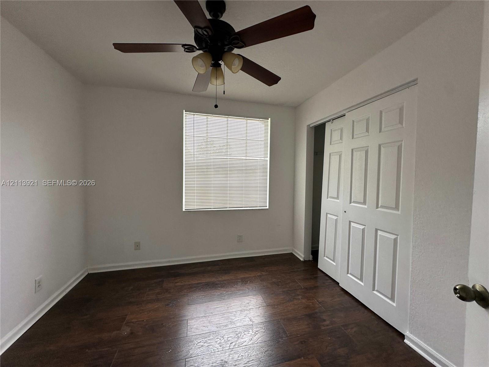 Wood-finish flooring, central ceiling fan with integrated lighting, multi-pane window, and white paneled sliding closet doors