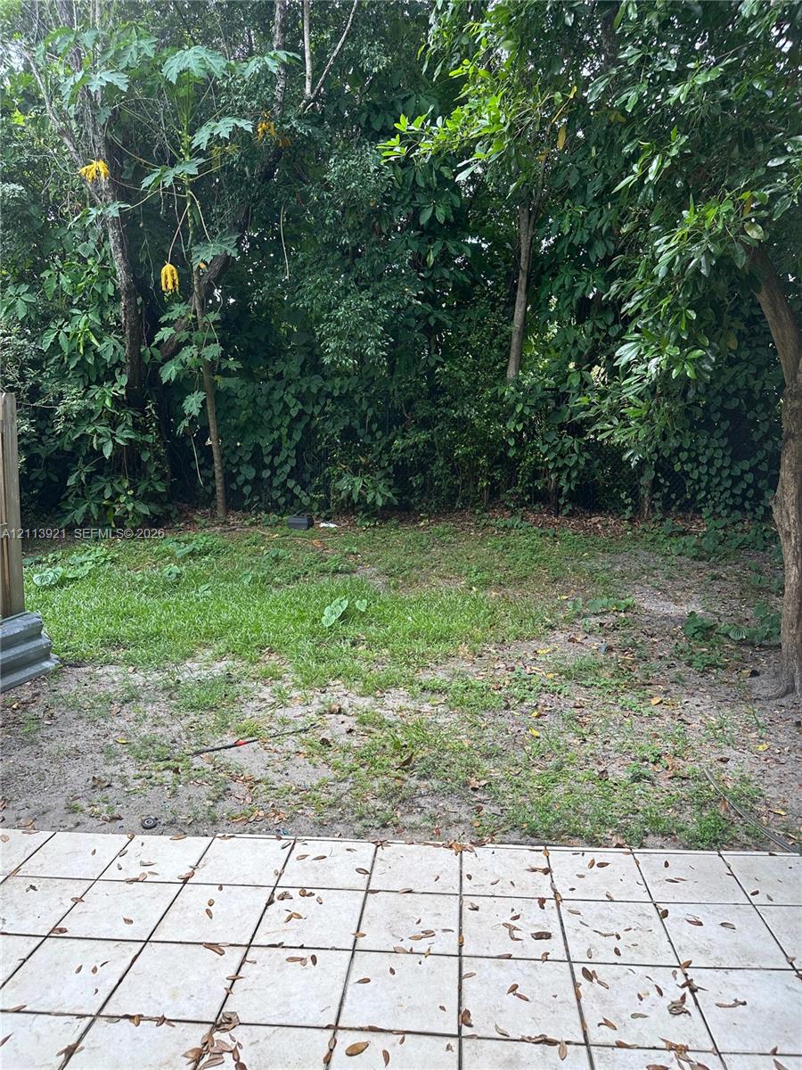 Outdoor patio featuring square ceramic tile flooring and a perimeter of mature trees and foliage