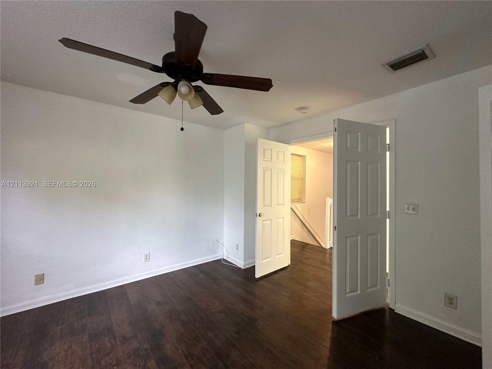 Room featuring wood-finish flooring, a six-panel door, and a ceiling fan with integrated lighting