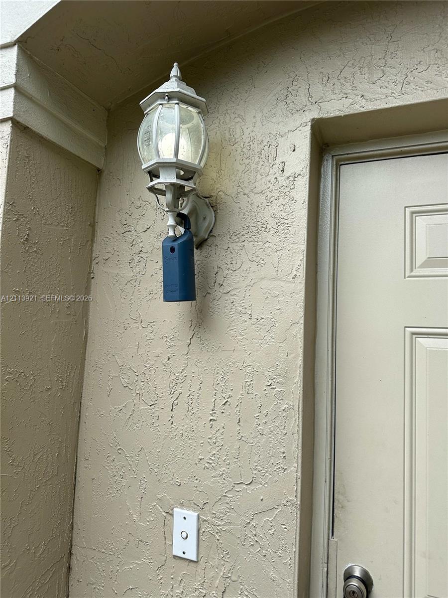 Exterior wall featuring a textured stucco finish, traditional carriage-style wall-mounted light fixture, and a solid-panel door with a metallic hardware finish