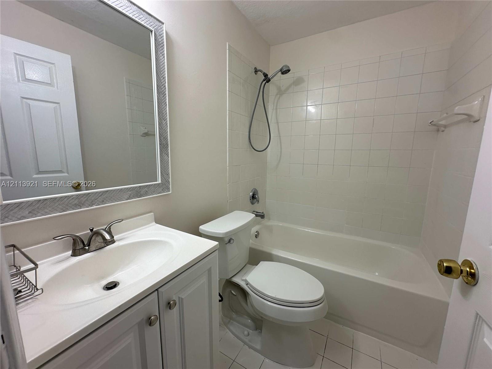 Bathroom featuring a white vanity cabinet, integrated sink with metallic dual-handle faucet, framed wall mirror, and tub-shower combination with tiled surround