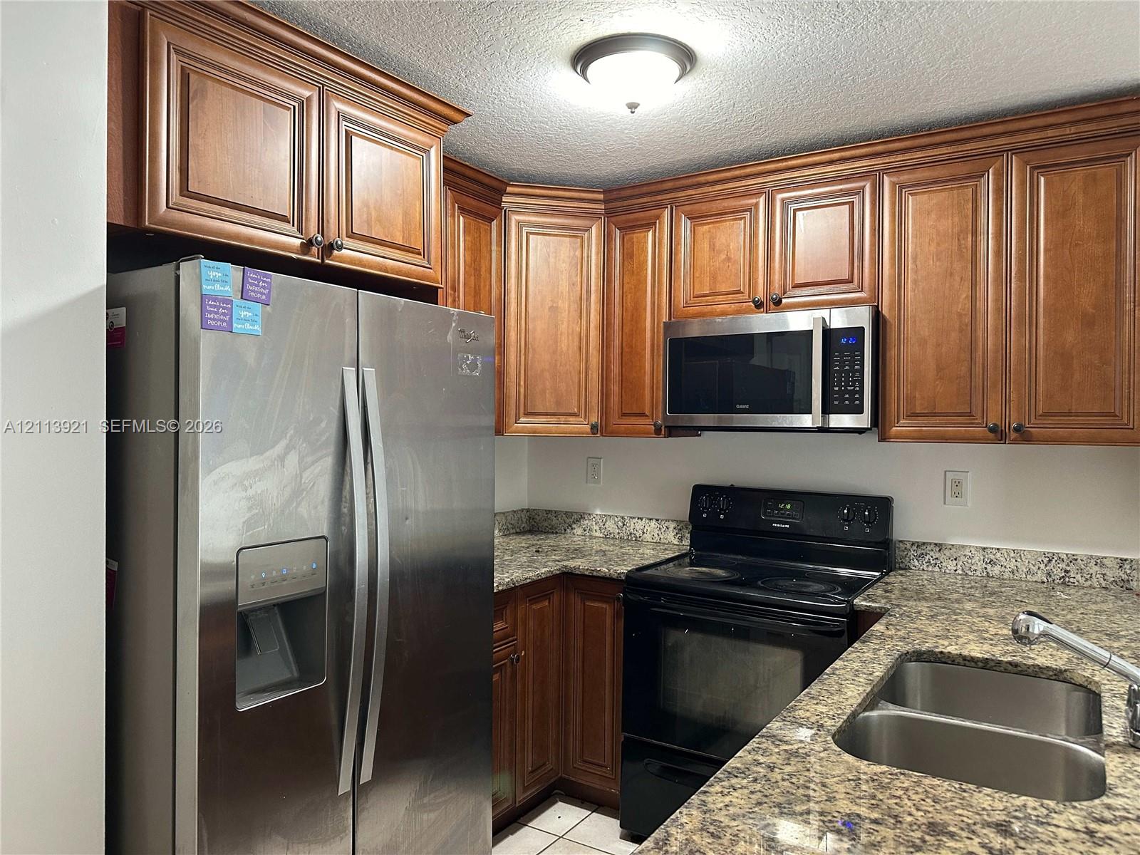 Kitchen featuring stained wood cabinetry, stone-patterned countertops, stainless steel side-by-side refrigerator, built-in microwave, and stainless steel dual-basin sink