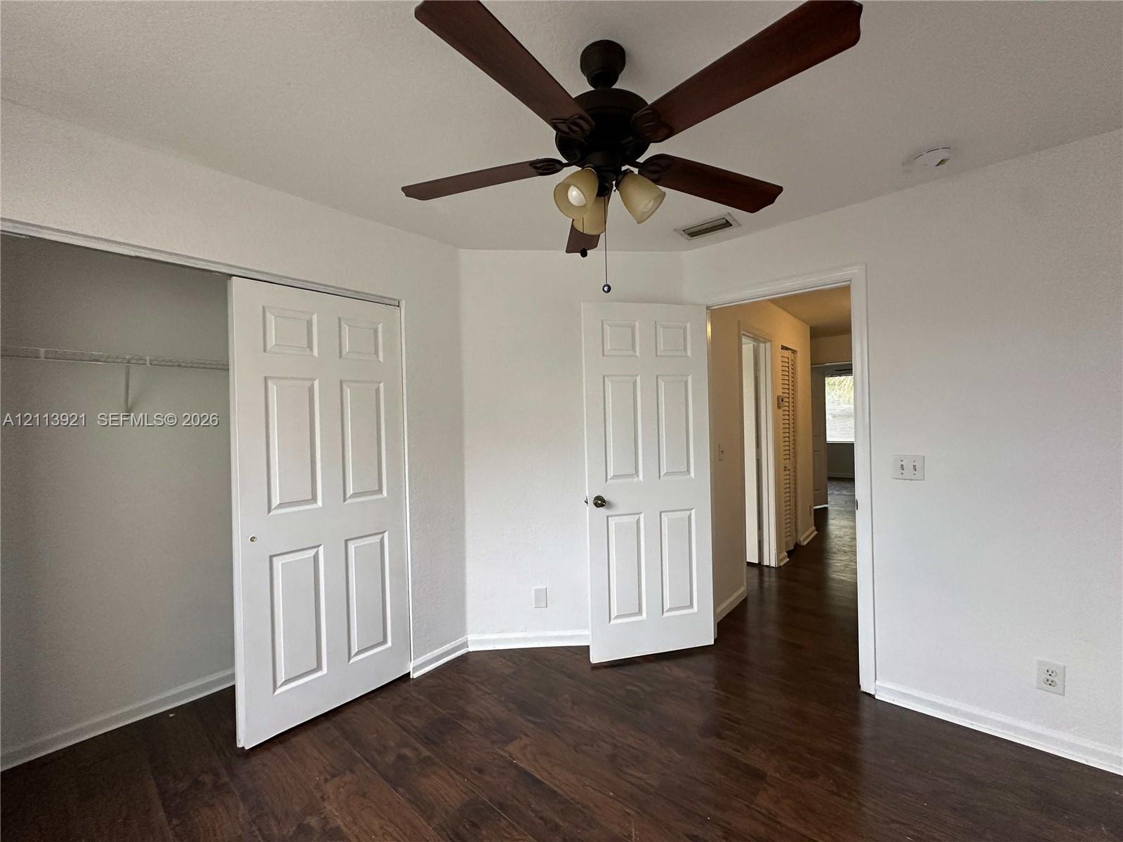 Wood-finish flooring, ceiling fan with integrated lighting, and multi-panel interior doors