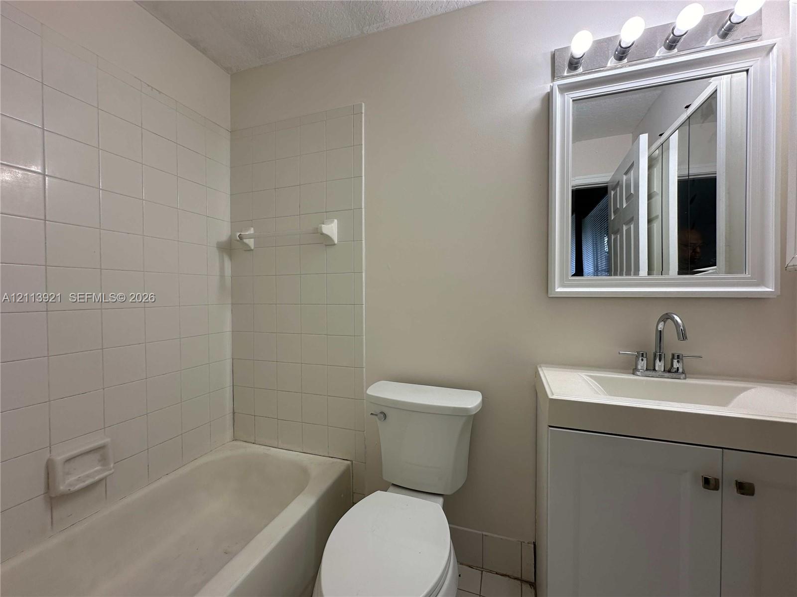 Bathroom featuring a white vanity with an integrated sink, polished chrome faucet, white square-tile shower surround, and a framed vanity mirror with an overhead multi-light fixture