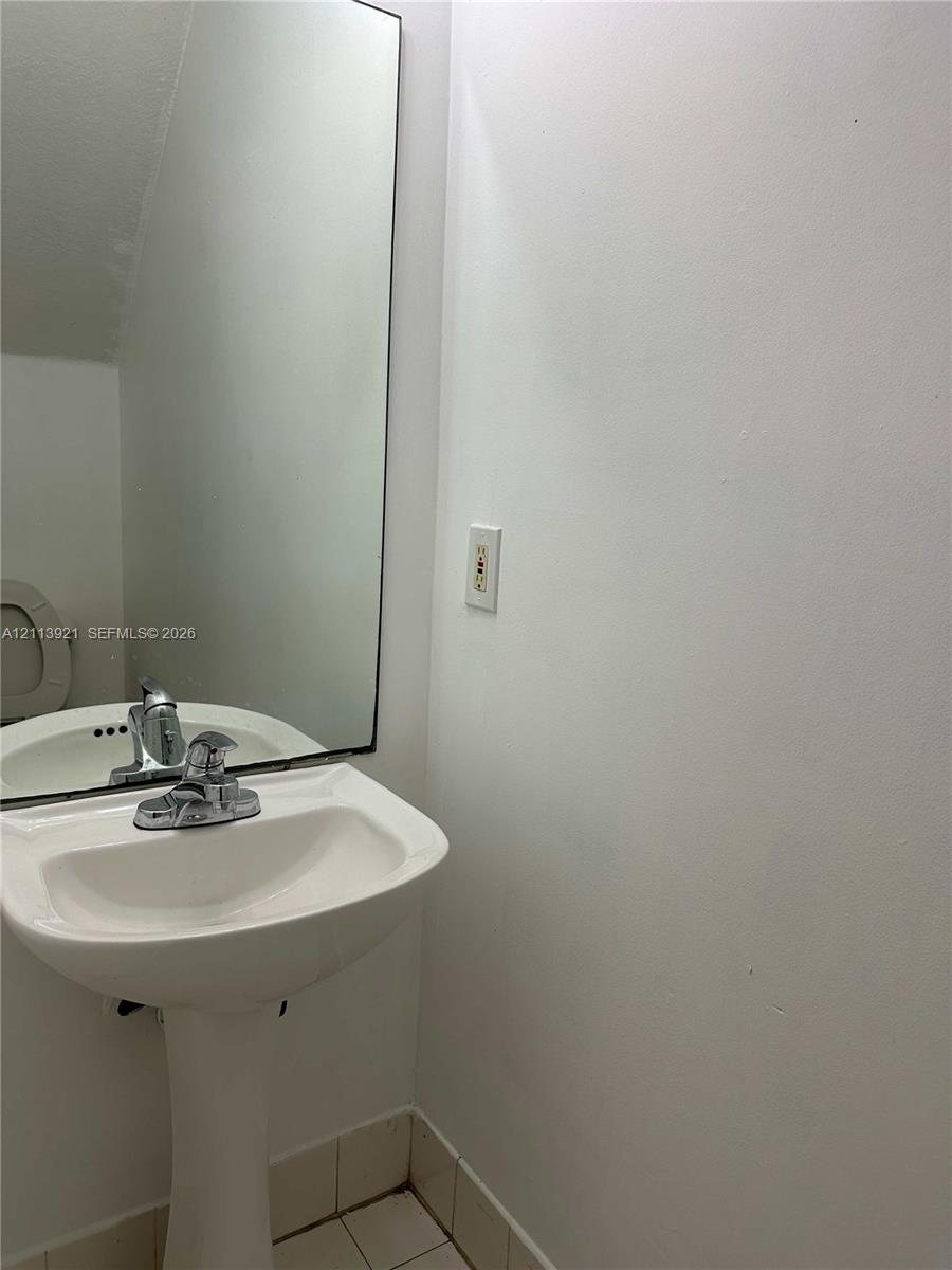 White pedestal sink featuring a chrome faucet, large rectangular mirror, and neutral tile flooring
