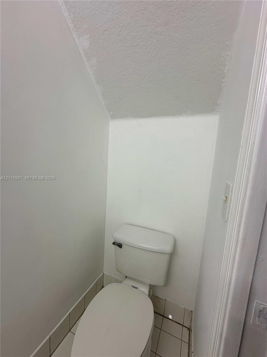 White toilet with an elongated bowl, tile flooring, and angled ceiling