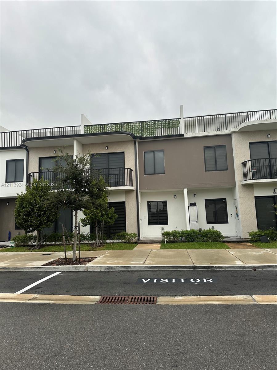 Modern multi-level exterior featuring stucco siding, upper-level balconies with metal railings, a flat roof deck with perimeter fencing, and expansive glass sliding doors