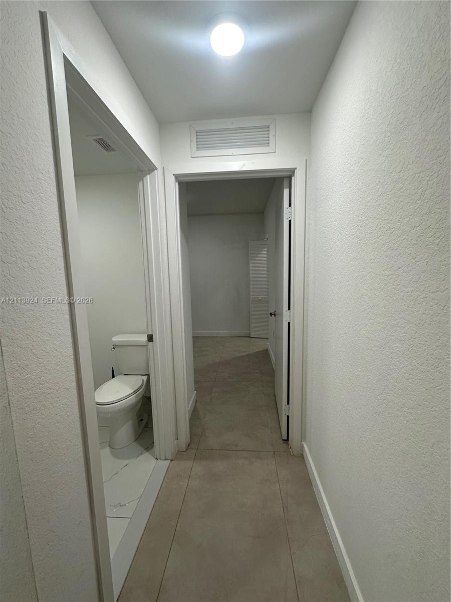 Neutral-toned tile flooring, flush-mount ceiling lighting, and a white two-piece toilet
