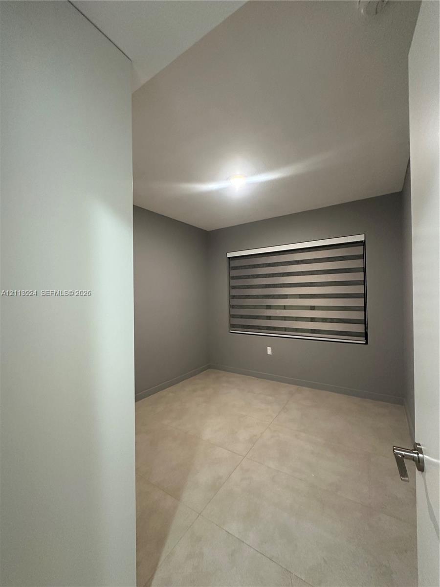 Neutral-toned interior space featuring large-format tile flooring, grey wall finish, and a window equipped with horizontal zebra-style blinds