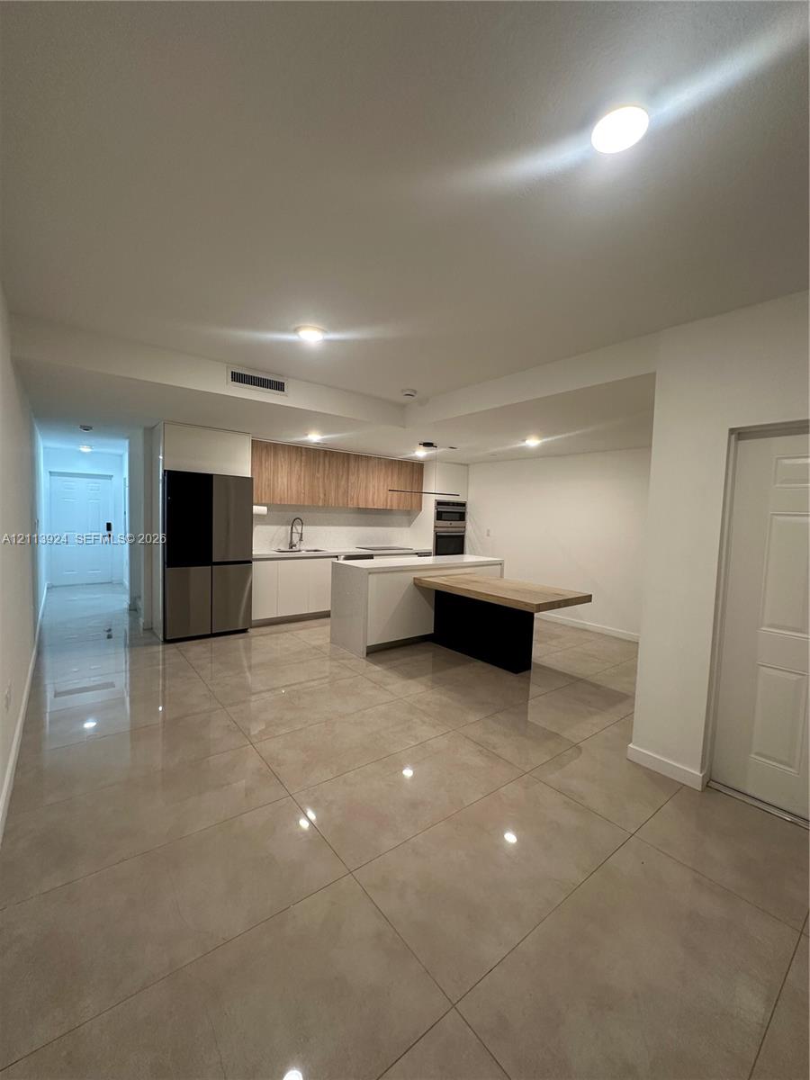 Kitchen featuring high-gloss cabinetry, wood-finish upper cabinets, integrated stainless steel appliances, a center island with an attached breakfast bar, and polished tile flooring