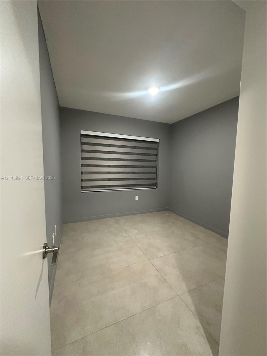 Neutral-toned interior room featuring large-format tile flooring, gray walls, and a window equipped with banded roller shades