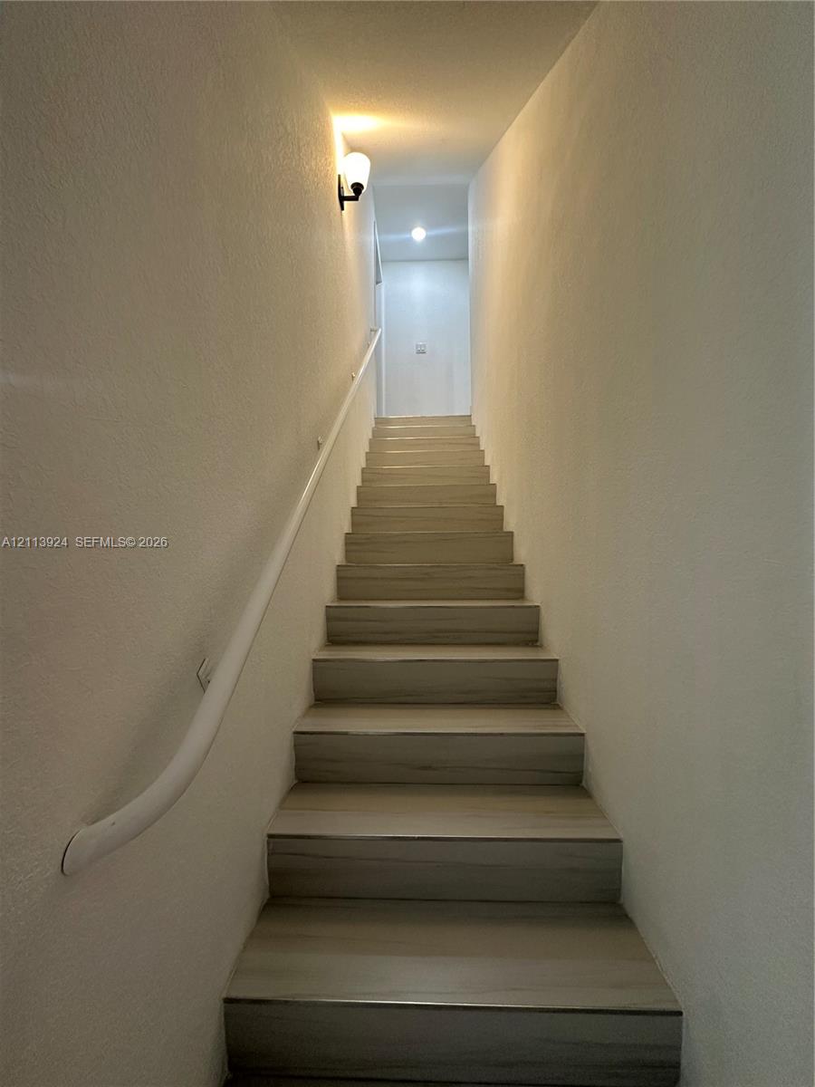 Staircase featuring wood-finish treads and a wall-mounted handrail