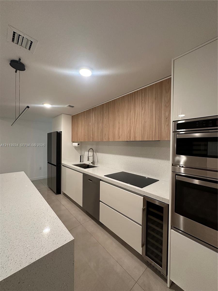 Contemporary kitchen featuring a stone-surface waterfall island, flat-panel cabinetry with wood-finish upper units, integrated stainless steel appliances, built-in beverage refrigerator, and solid-surface countertops