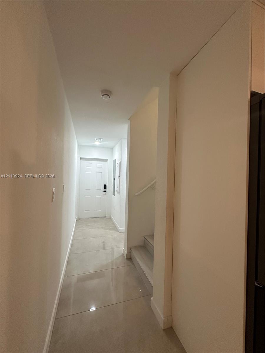 Hallway featuring large-format tile flooring, a six-panel exterior entry door, and a staircase with a mounted handrail