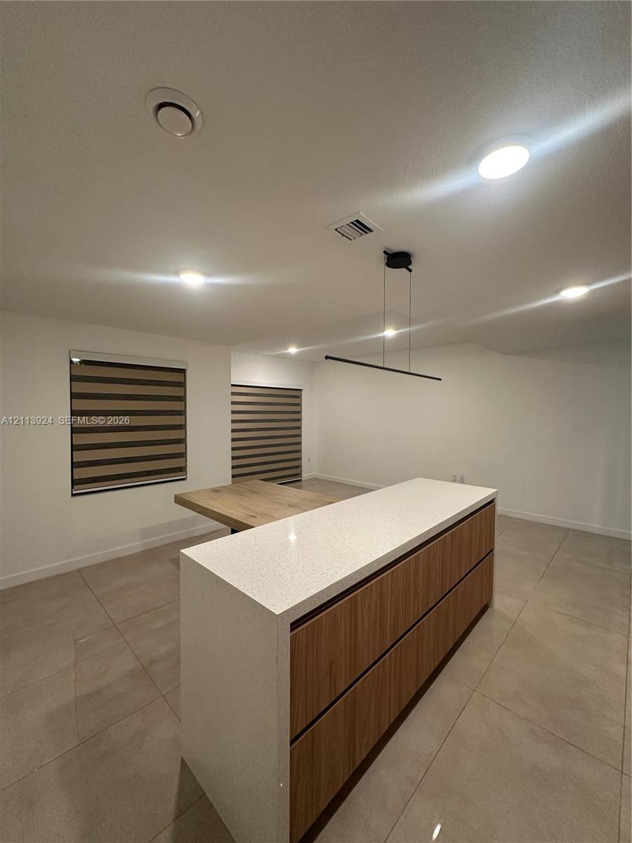Center island featuring a stone-look countertop, wood-finish cabinetry, built-in dining surface, recessed lighting, and modern linear pendant fixture