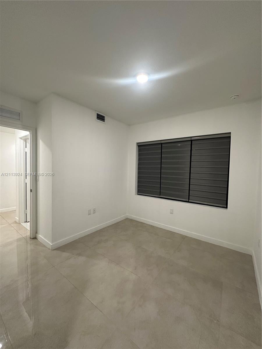 Neutral interior featuring large-format ceramic tile flooring, solid white walls, and a recessed window with installed horizontal dual-shade blinds