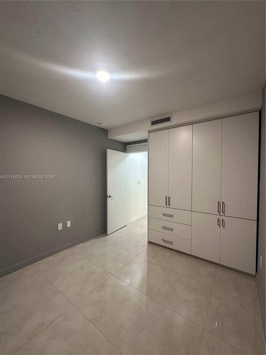 Room featuring large-format tile flooring, built-in floor-to-ceiling white cabinetry with integrated drawers, and a ceiling-mounted light fixture