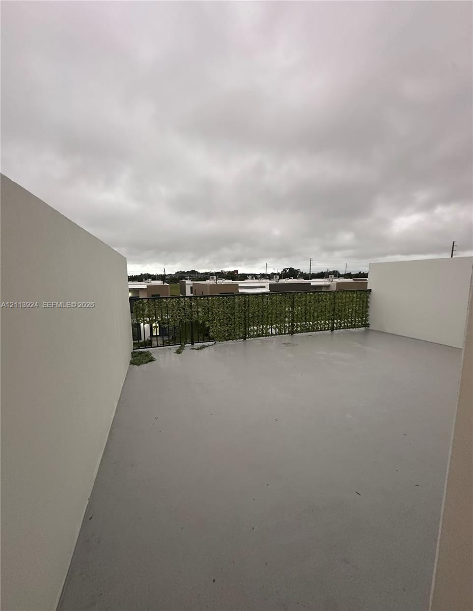 Rooftop terrace featuring smooth concrete flooring, solid privacy walls, and a metal railing with integrated greenery