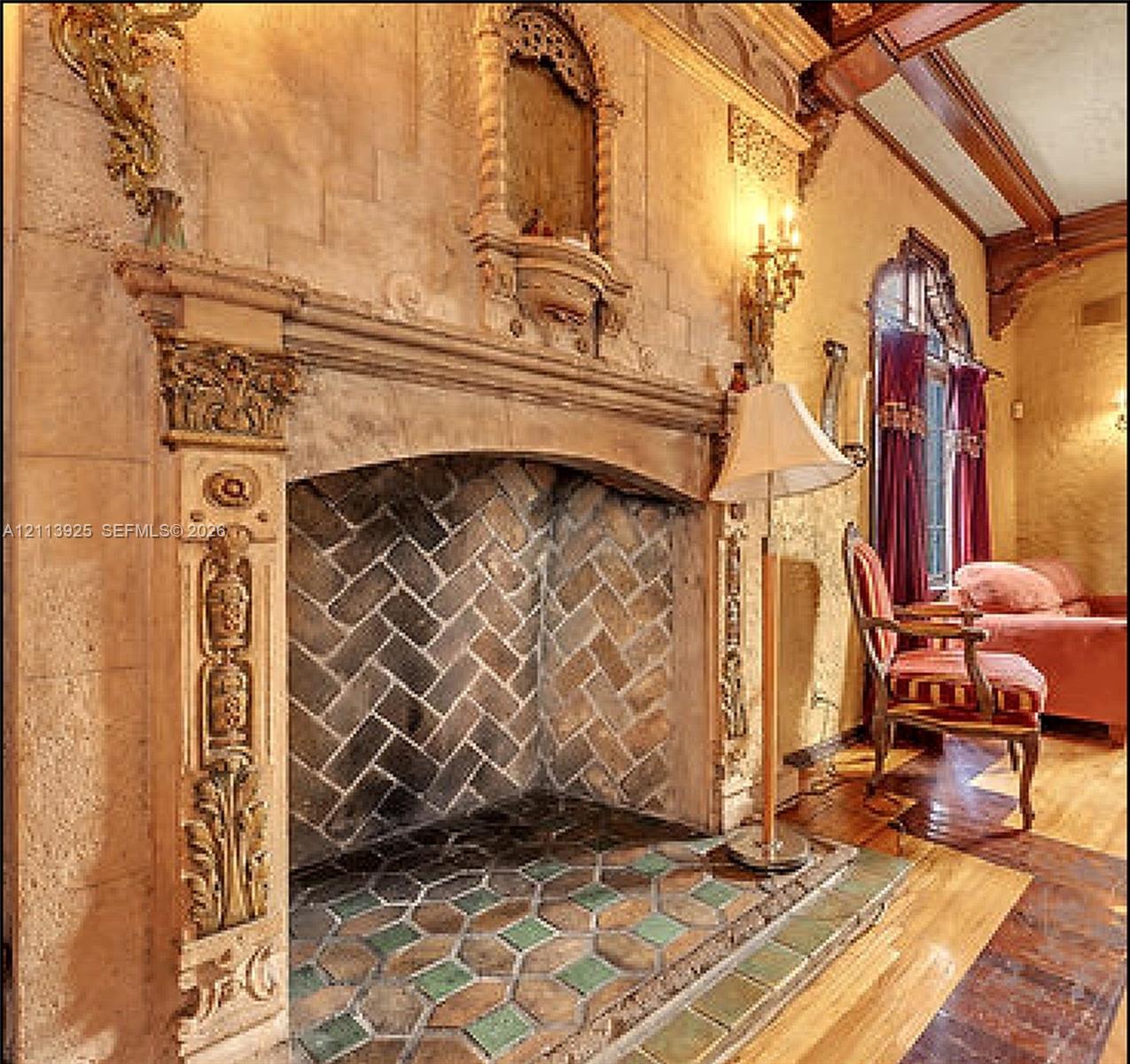 Ornate fireplace featuring carved masonry detailing, a herringbone-pattern firebox, decorative tile hearth, and wood-beam ceiling
