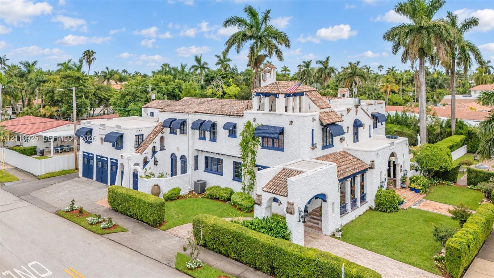 Spanish Colonial Revival exterior featuring a multi-level silhouette, textured white masonry, clay tile roofing, arched entryway, and blue metal window awnings