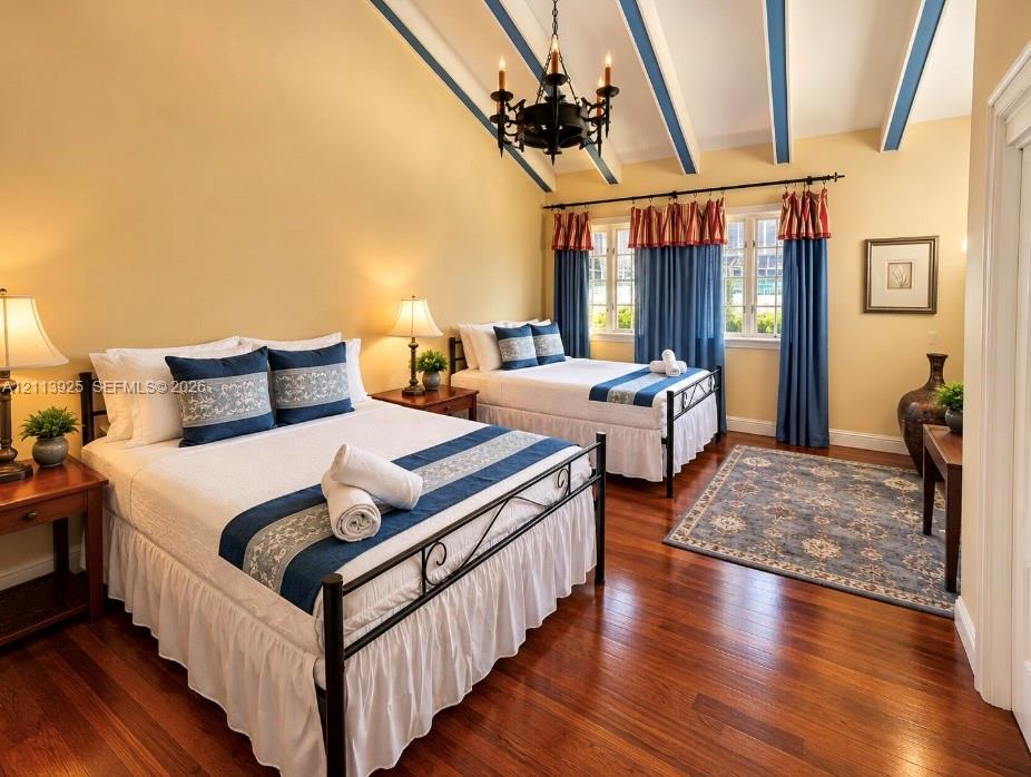 Vaulted ceiling with exposed decorative beams, iron chandelier, and polished wood-finish flooring