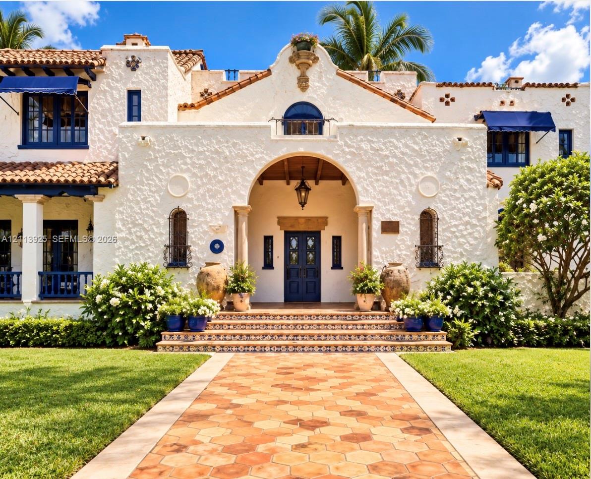 Spanish Revival exterior featuring a textured stucco facade, red tile roof, arched entryway, ornate tiled stairs, and a hexagonal paver walkway