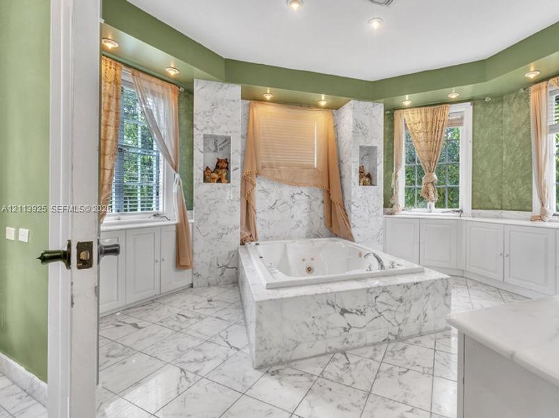 Stone-surround jetted soaking tub, custom stone flooring, built-in shelving niches, recessed lighting, and expansive wrap-around cabinetry