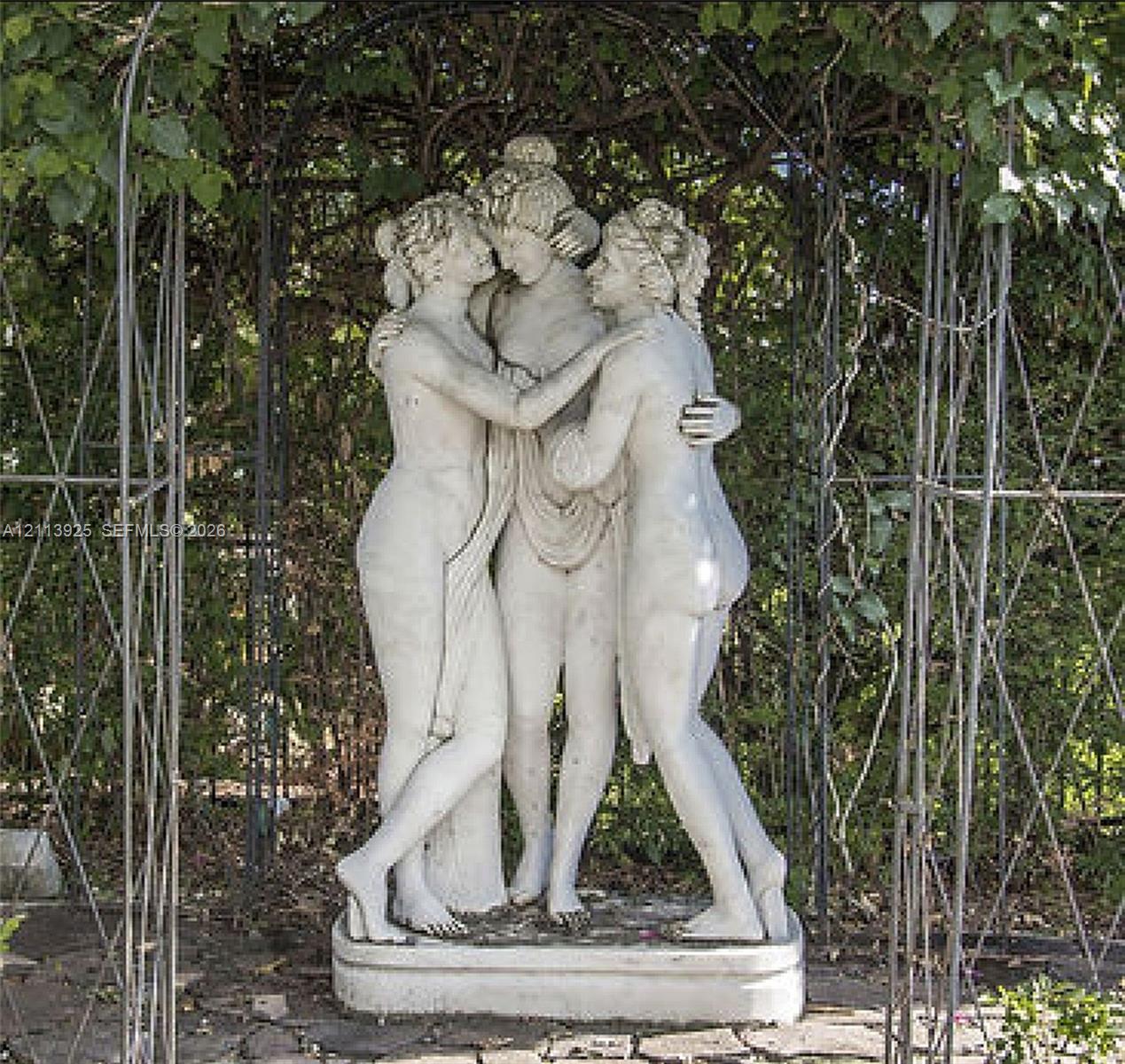 Ornate stone figurative sculpture positioned beneath a metal garden trellis