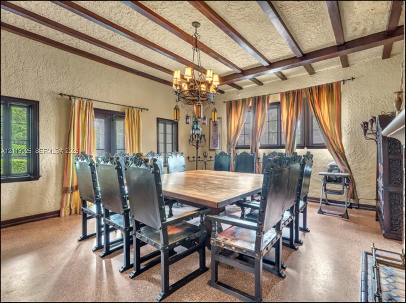 Exposed dark wood ceiling beams, textured plaster walls, wrought-iron multi-tier chandelier, and tile flooring