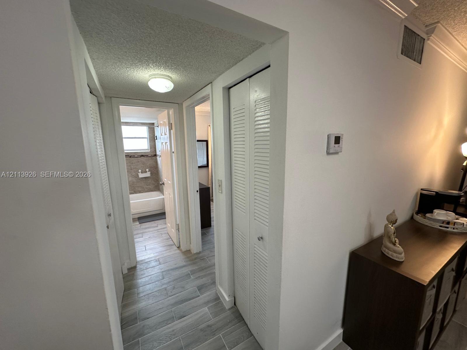 Hallway featuring wood-finish tile flooring, multiple louvered-door closets, and crown molding