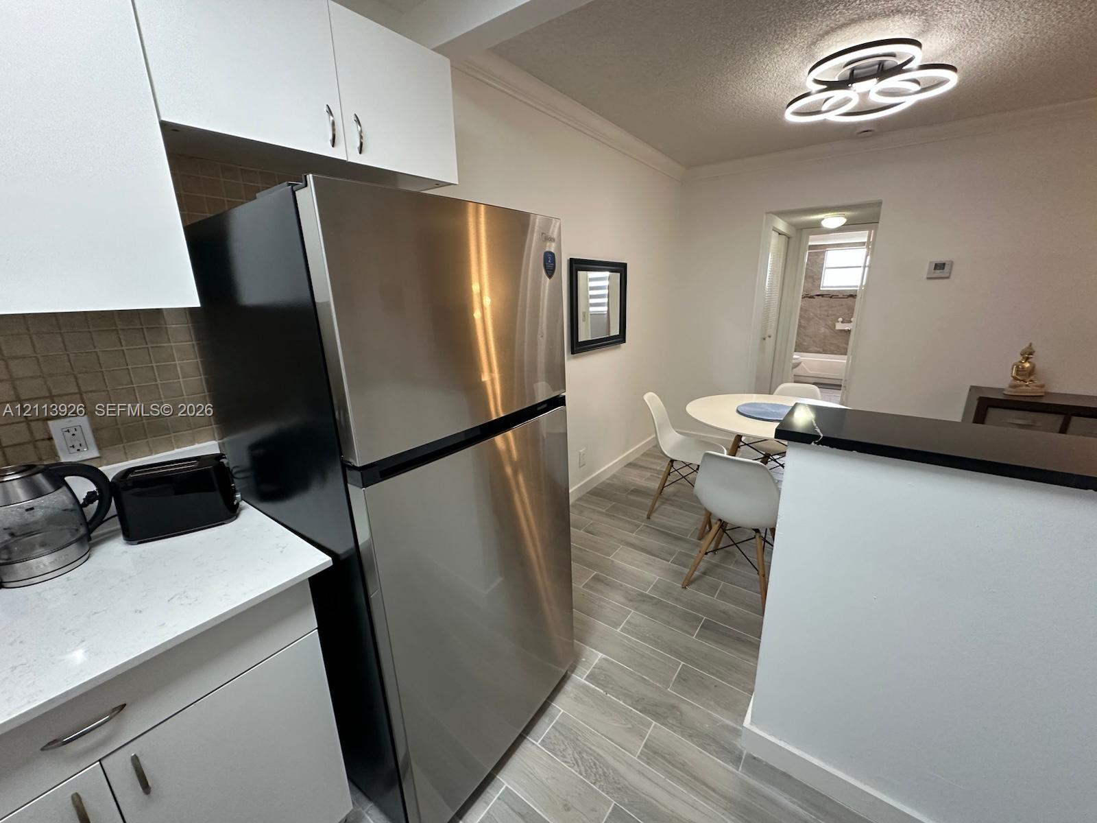 Kitchen featuring white cabinetry, solid-surface countertops, tile backsplash, stainless steel refrigerator, and wood-finish flooring