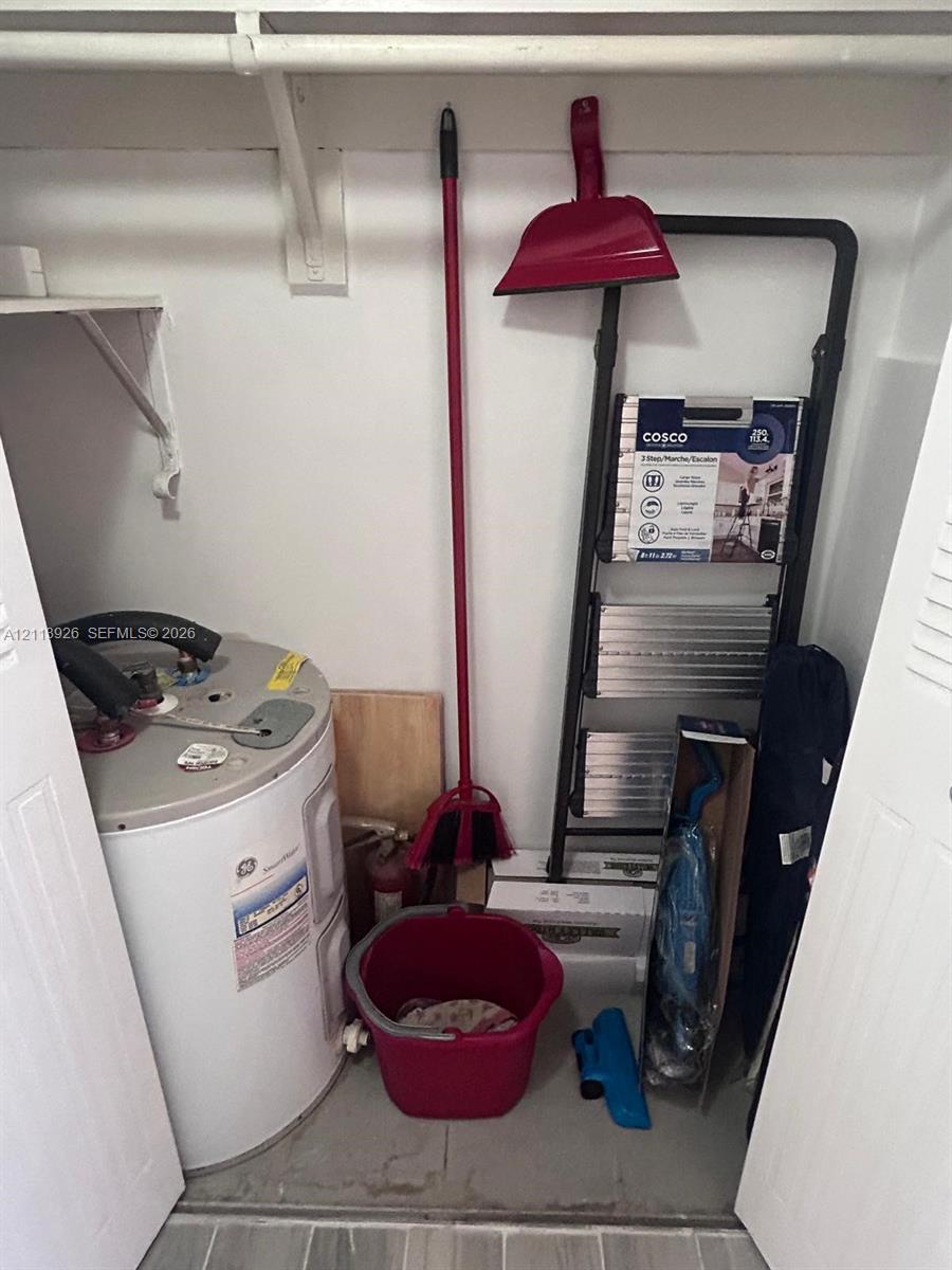 Utility closet featuring an electric water heater, built-in shelving, and a hanging rod